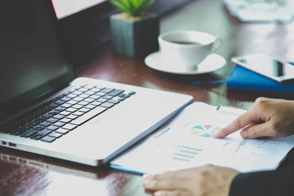 Financial analyst with document in his hands reading information on computer screen