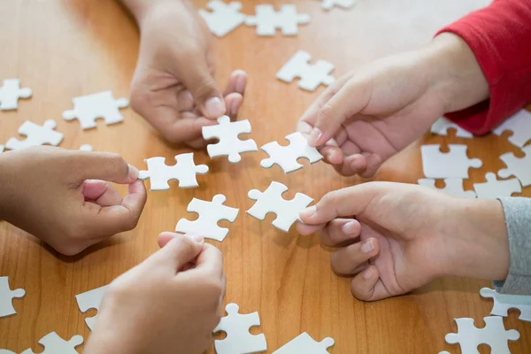 Hands of diverse people assembling jigsaw puzzle, team put pieces together searching for right match, help support in teamwork to find common solution concept, top close up view