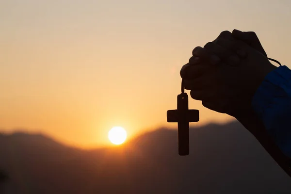 Silhueta de mulher jovem cristã rezando com uma cruz ao sol — Fotografia de Stock