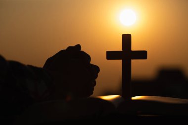 Silhouette of young woman praying with crosses and bibles at sun clipart