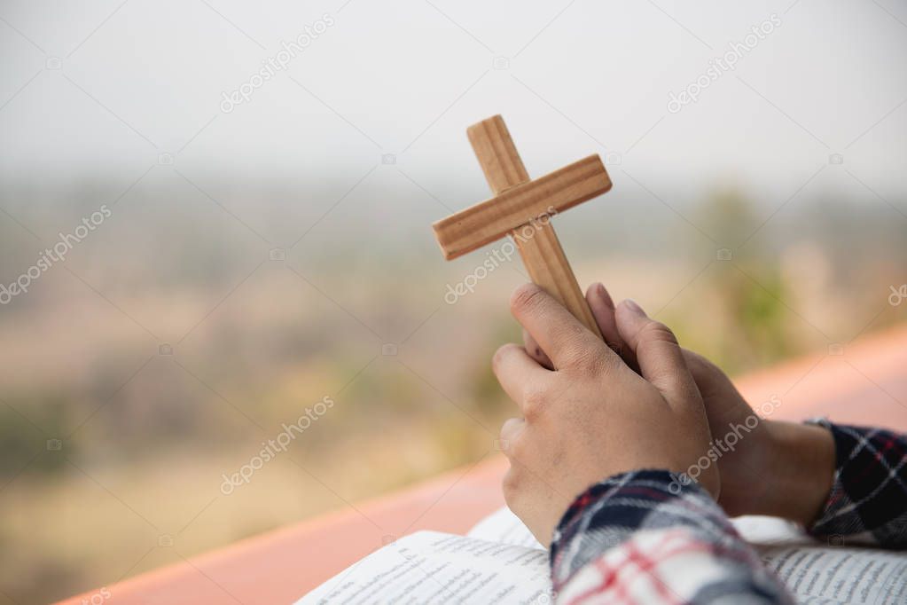 close up young hands holding wooden cross over holy bible and pr
