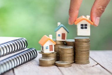 İnsan eli ev modelini madeni para yığınına koyar, tasarruf yapmayı planlar.