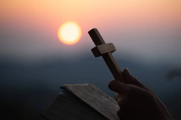 Manos sosteniendo la cruz de madera sobre la sagrada Biblia abierta en la montaña — Foto de Stock