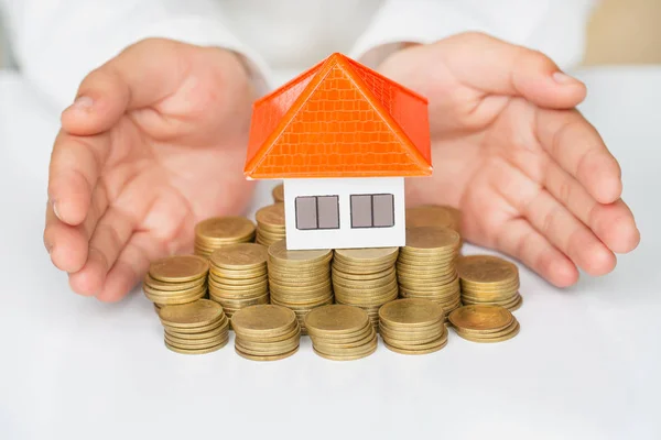 Woman hand protecting on stack coins and house model on table,