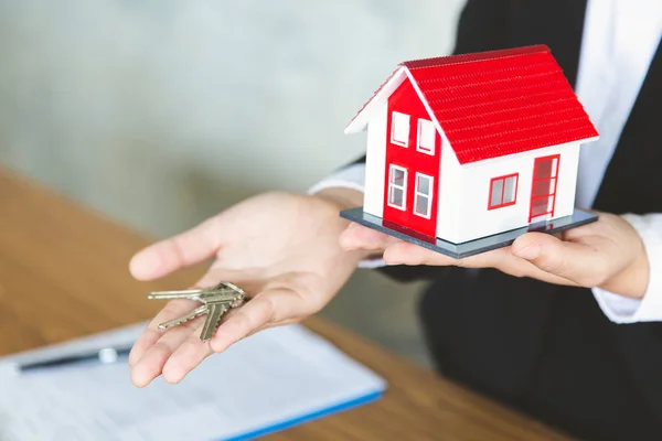 Immobilienmakler hält Hausmodell und Schlüssel, Kunde meldet sich an — Stockfoto