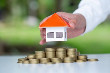 İnsan eli ev modelini madeni para yığınına koyar, tasarruf yapmayı planlar.