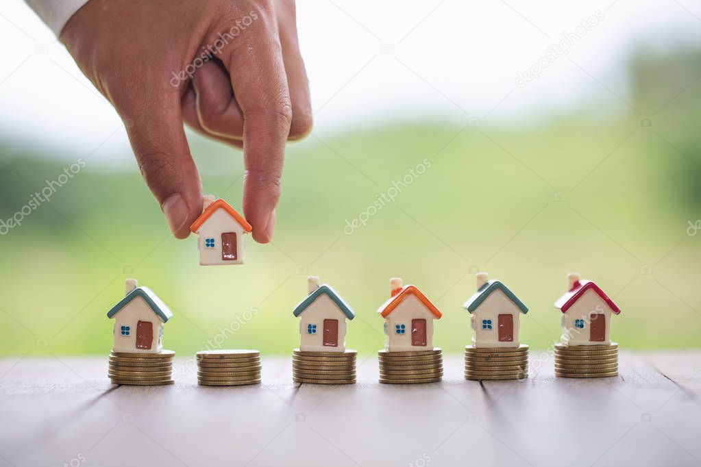 Woman's hand putting house model on coins stack. Concept for pro