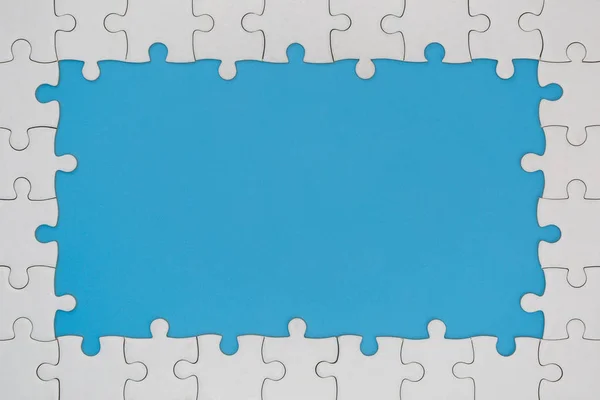 Unfinished white jigsaw puzzle pieces on blue background, The la