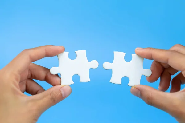 Business woman hand is trying to connect couple White jigsaw puzzle piece on a blue background. Symbol of association and connection. Concept of business strategy.