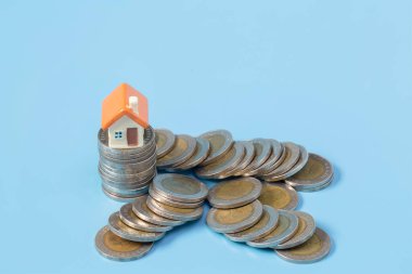 Mavi arka planda küçük bir ev dolusu bozuk para. Yatırım mülkiyeti kavramı. Para biriktirmek, gayrimenkule yatırım yapmak..