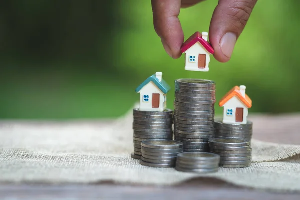 Woman\'s hand putting house model on coins stack. Concept for property ladder, planning savings money of coins to buy a home concept property mortgage and investment for a house.