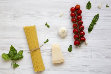 Spagetti, domates, fesleğen, parmesan, sarımsak. Beyaz ahşap bir masa, düz pişirme makarna için malzemeler yatıyordu. Yukarıdan.