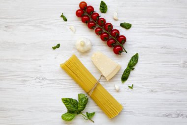 Spagetti, domates, fesleğen, parmesan, sarımsak. Maddeler üzerinde beyaz bir ahşap masa, düz İtalyan makarna yemek pişirmek için yatıyordu. Yukarıdan.