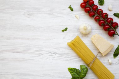 Spagetti, domates, fesleğen, parmesan, sarımsak. Beyaz ahşap bir masa, düz pişirme makarna için malzemeler yatıyordu. Yukarıdan. Kopya alanı.