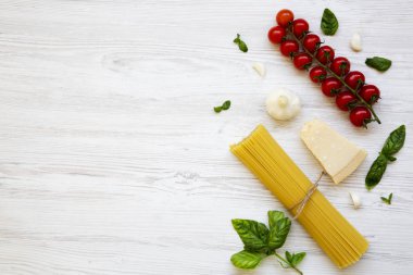 Spagetti, domates, fesleğen, parmesan, sarımsak. Beyaz ahşap bir masa, düz pişirme makarna için malzemeler yatıyordu. Yukarıdan. Kopya alanı.