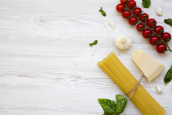 Spaghetti, tomatoes, basil, parmesan, garlic. Ingredients for cooking pasta on a white wooden table, flat lay. From above. Copy space.