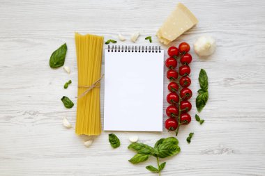 Beyaz ahşap arka planda, üstten görünüm makarna yemek pişirmek için malzemeler ile defter. Uzay kopyalayın. Düz yatıyordu.