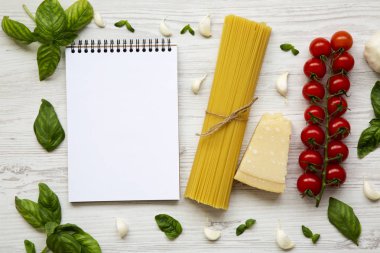 Spagetti, parmesan, domates, sarımsak ve Beyaz ahşap arka planda, üstten görünüm fesleğen ile defter. Uzay kopyalayın. Düz yatıyordu.