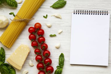 Beyaz ahşap zemin üzerinde defter ile İtalyan makarna yemek pişirmek için malzemeler. Düz yatıyordu. Portre. Üstten Görünüm. Kopya alanı