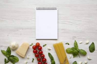 Beyaz ahşap zemin üzerinde İtalyan makarna yemek pişirmek için malzemeler ile defter. Düz yatıyordu. Üstten Görünüm. Kopya alanı