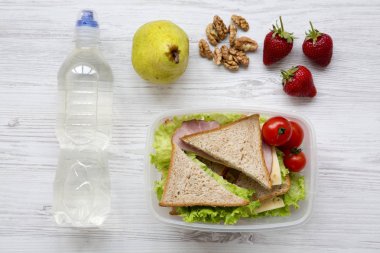 Sağlıklı okul öğle yemeği kutusu taze organik sebze sandviç, ceviz, meyve Beyaz ahşap zemin üzerinde ve su şişe, düz yatıyordu. Yukarıdan. Üstten Görünüm.