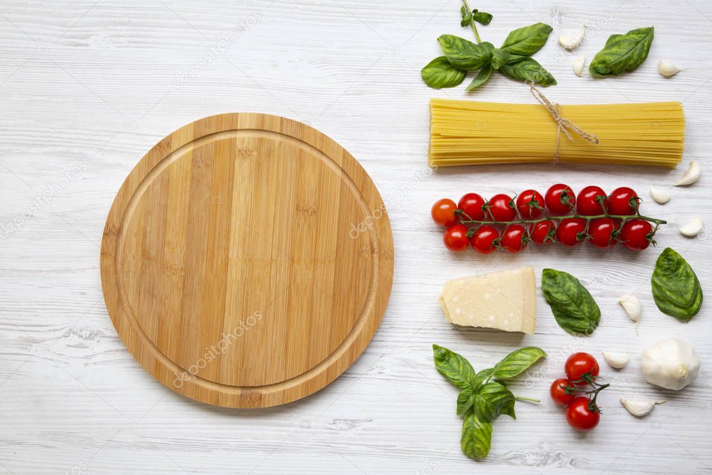 Round wooden board with ingredients for cooking pasta on a white wooden background, top view. Flat lay. Copy space.