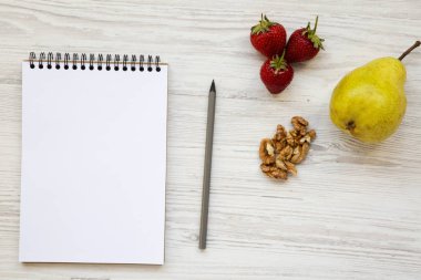 Çalışma alanı için sağlıklı kişi: defter, kalem, ceviz, çilek ve armut beyaz ahşap zemin üzerinde. Yukarıdan, yatıyordu, en iyi görünüm düz.