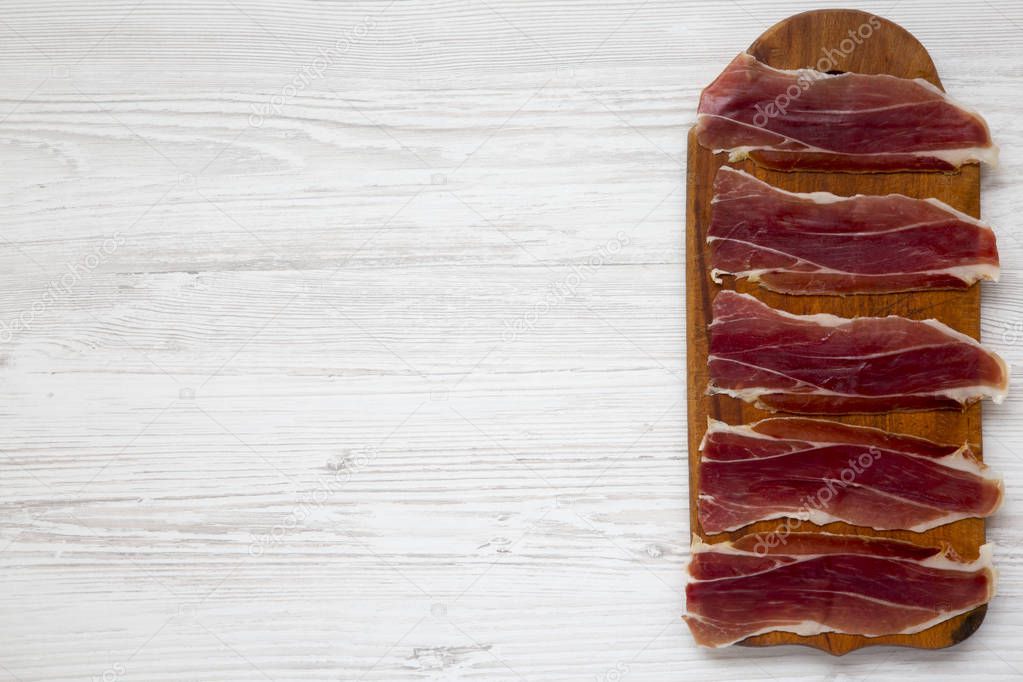 Sliced jamon Serrano or Iberico on cutting wooden board. Traditional spanish hamon on white wooden background, top view. Copy space.