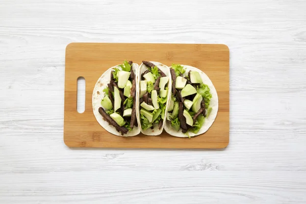 Mexican tacos on the bamboo board on a white wooden background, top view. Flat lay, from above.