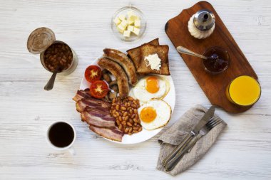 Tam İngiliz kahvaltısı kızarmış yumurta, pastırma, sosis, fasulye ve tost Beyaz ahşap arka planda, üstten görünüm ile. Düz yatıyordu. Yukarıdan.