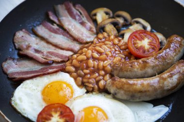 Bir tavada kızarmış yumurta, pastırma, sosis, fasulye ve tost ile İngiliz kahvaltısı. Portre.