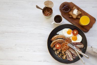 Tam İngiliz kahvaltısı bir tavada kızarmış yumurta, pastırma, sosis, fasulye ve tost Beyaz ahşap arka planda, üstten görünüm ile. Uzay kopyalayın. Düz yatıyordu. Yukarıdan. 