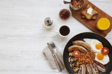 Tam İngiliz kahvaltısı bir tavada kızarmış yumurta, pastırma, fasulye, sosis ve tost Beyaz ahşap arka planda, üstten görünüm ile. Düz yatıyordu. Yukarıdan. Kopya alanı. 