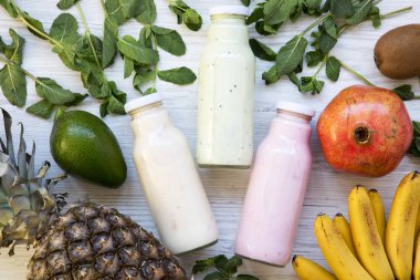 Beyaz ahşap zemin üzerinde malzemelerle cam kavanozlara farklı tadı meyve smoothies. En iyi manzara, yukarıda. Düz yatıyordu. 