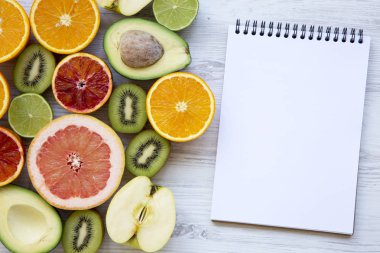 Üstten görünüm beyaz tahta masada boş not defteri ile farklı taze meyve. Yaz arka plan. Kopya alanı.