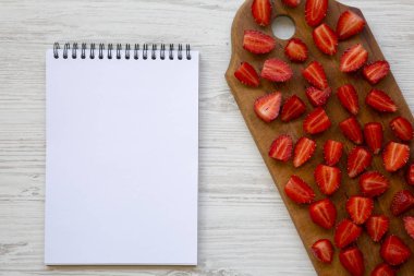 Ahşap masa ve boş not defteri, üstten görünüm üzerinde taze çilek. Uzay kopyalayın. Beyaz ahşap masa. Yukarıdan, lay düz.
