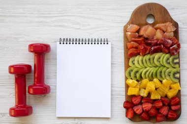 Fitness kavramı, diyet planı. kıyılmış meyve, halter, not etmek üstünde beyaz ahşap arka plan, üstten görünüm.