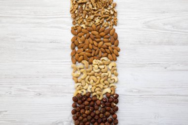 Beyaz ahşap zemin üzerinde fındık ürün yelpazesine. Kaju fıstığı, fındık, ceviz, badem. Üstten görünüm, düz yatıyordu. Kopya alanı. 