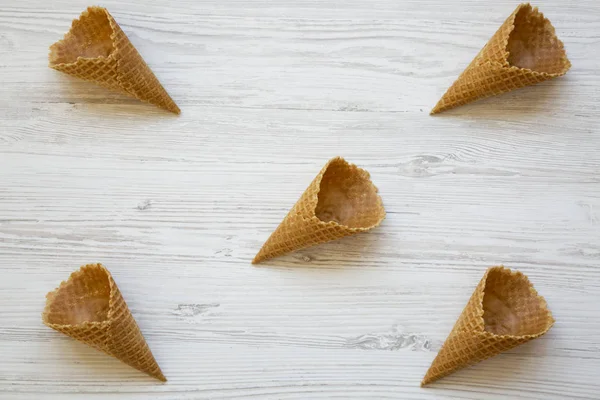 Waffle sweet cones over white wooden background, top view.