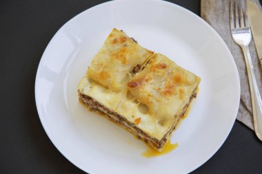Geleneksel sığır eti lazanya bir beyaz yuvarlak tabak, koyu arka plan, üstten görünüm. 