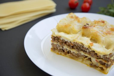 Lazanya bir beyaz tabak, koyu arka plan, yan görünüm.