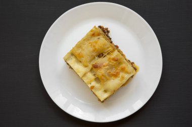 Geleneksel sığır eti lazanya bir beyaz üzerine siyah arka plan, üstten görünüm tabağa yuvarlak. Düz yatıyordu. Yukarıdan.