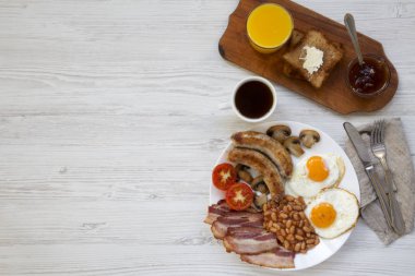 Sahanda yumurta, sosis, pastırma, fasulye ve tost ile düz yatıyordu, tam İngiliz kahvaltısı. Beyaz ahşap arka plan. Üstten görünüm. Kopya alanı.