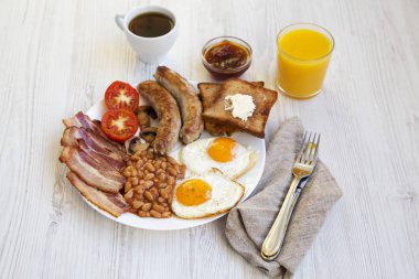 Yan görünüm, sahanda yumurta, sosis, pastırma, fasulye ve tost ile tam İngiliz kahvaltısı. Beyaz ahşap arka plan. Yakın çekim. 