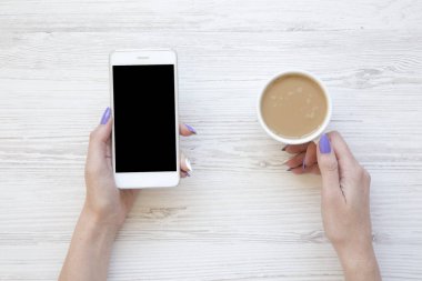 Smartphone kullanarak ve latte Beyaz ahşap arka plan üzerinde yukarıdan içme eller. Düz yatıyordu.