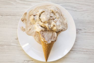 Dondurma külahı beyaz tabakta. Kaşık toz erime. Beyaz ahşap arka plan. Üstten görünüm. Yukarıdan, lay düz. 