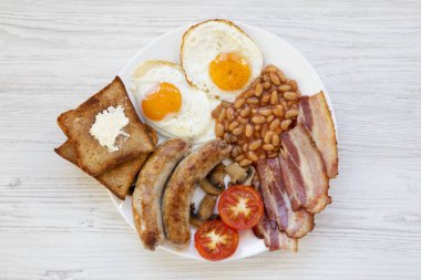 Sahanda yumurta, sosis, fasulye, pastırma ve beyaz ahşap zemin üzerinde tost ile İngiliz kahvaltısı. Üstten görünüm. Düz yatıyordu. Yukarıda, ek yükü.