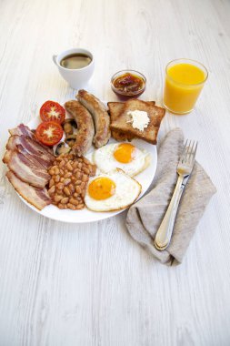 Tam İngiliz kahvaltısı kızarmış yumurta, pastırma, sosis, fasulye ve tost ile düz yatıyordu. Beyaz ahşap zemin. 