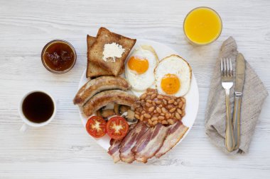 Tam İngiliz kahvaltısı kızarmış yumurta, pastırma, sosis, fasulye ve tost Beyaz ahşap arka planda, üstten görünüm ile beyaz yuvarlak tabakta. Düz yatıyordu. Yukarıdan.