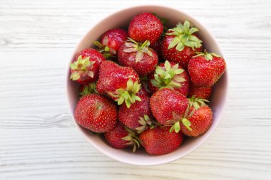 Beyaz ahşap masa, üstten görünüm üzerinde pembe bir seramik kase taze çilek. Yukarıdan.